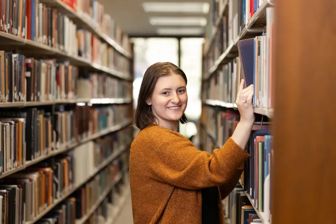 Student inside of library choosing book from shelf.